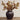 Artificial oak leaf arrangement in a dark brown ceramic vase, displayed on a rustic wooden surface against a light beige paneled wall.