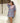 Woman wearing a  short blue and pink floral dress standing against a white wall.